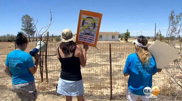 People holding protest signs at a fenced installation